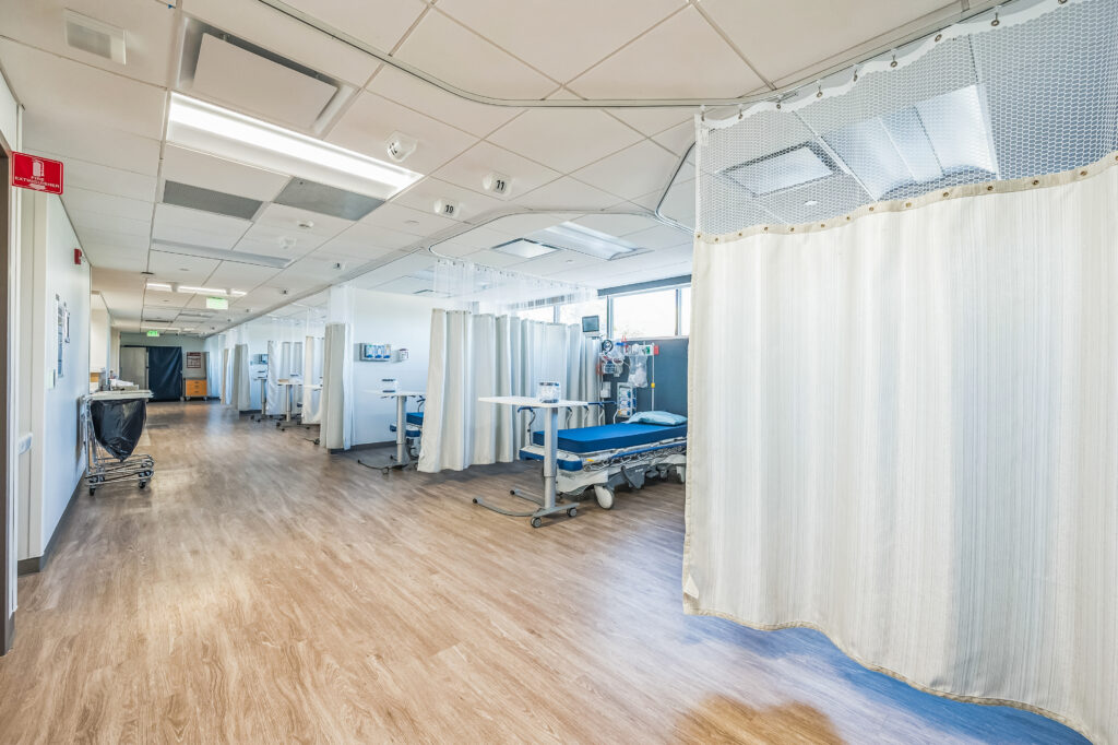 A row of hospital bays with beds and privacy curtains in a medical facility.