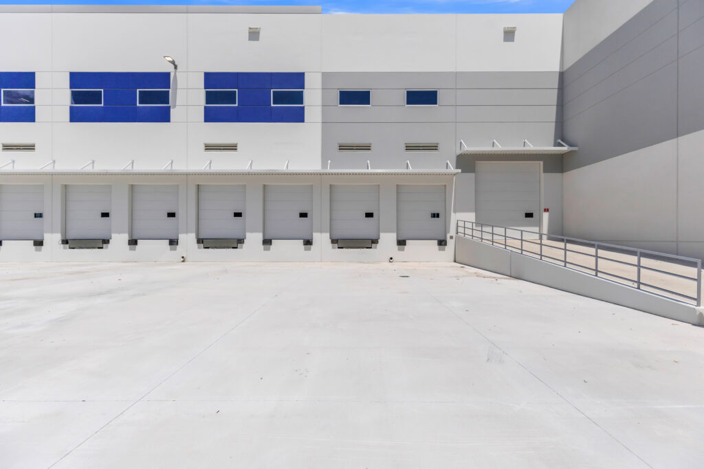 Exterior of a modern industrial warehouse with six loading docks and a wheelchair-accessible ramp.