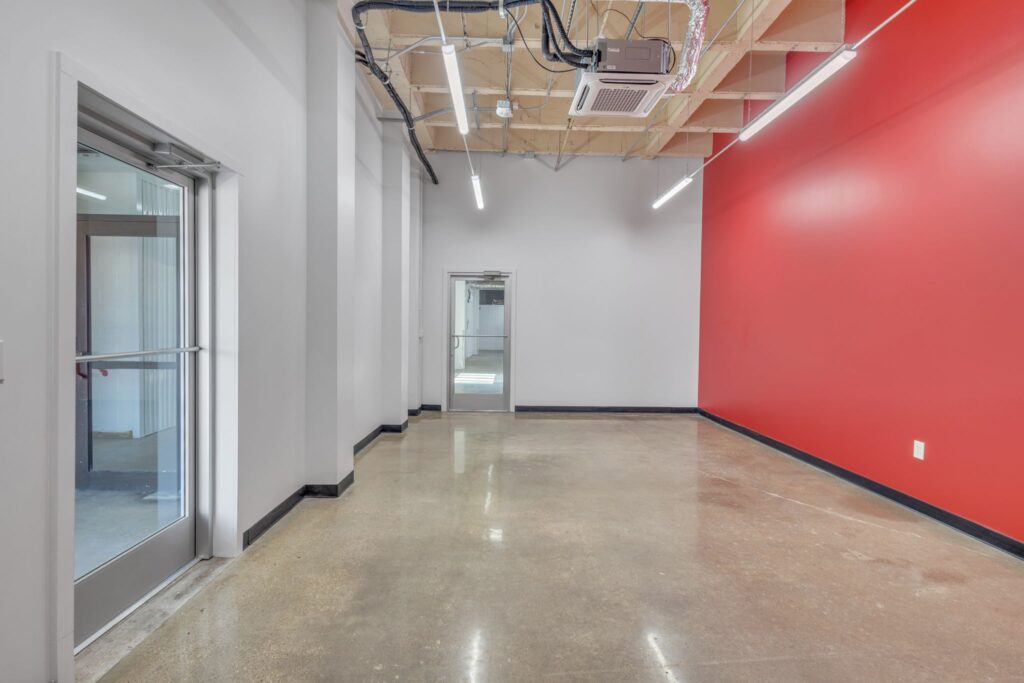 An empty office space with polished concrete floors, white walls, and one accent wall painted bright red.