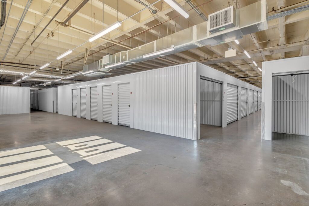 Indoor storage facility featuring rows of white metal roll-up storage units with one unit door standing open.