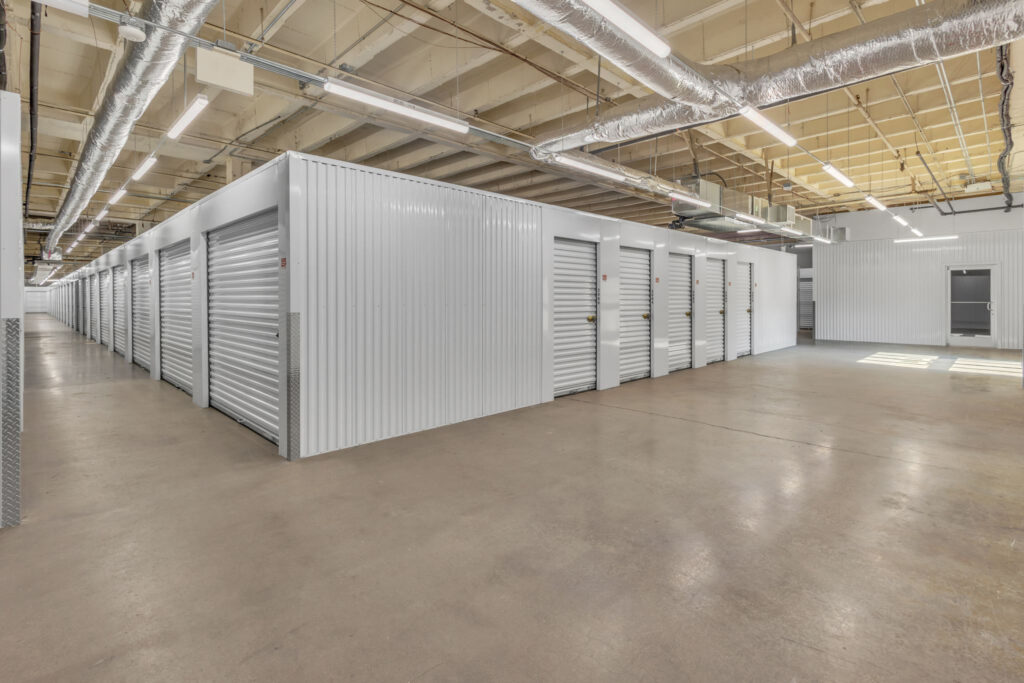 A long indoor hallway in a self-storage facility featuring rows of white metal roll-up storage unit doors.