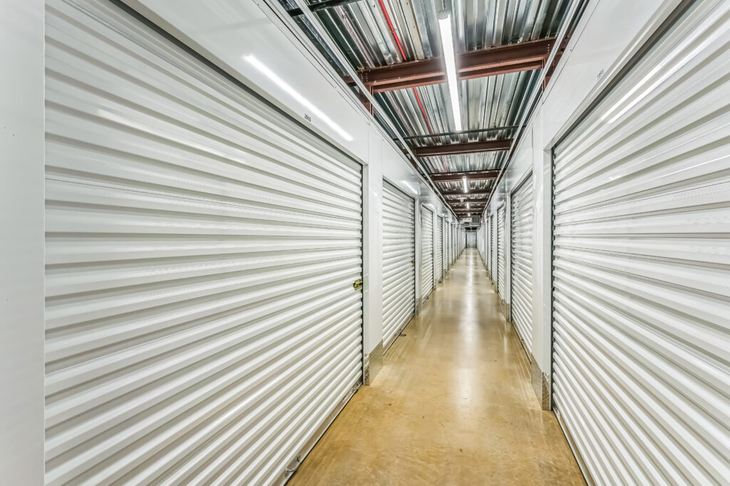 A long, narrow hallway lined with rows of closed white metal storage unit doors on both sides.