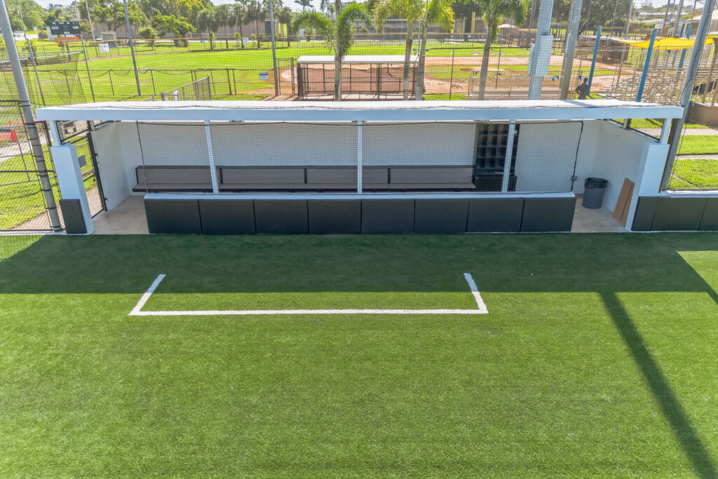 An outdoor baseball dugout with bench seating, located on a turf field with white foul lines.