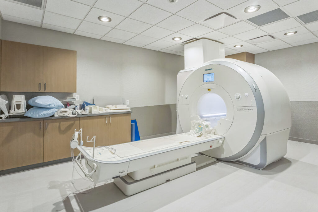 An MRI scanner in a medical imaging room with a patient bed extended in front of the machine.