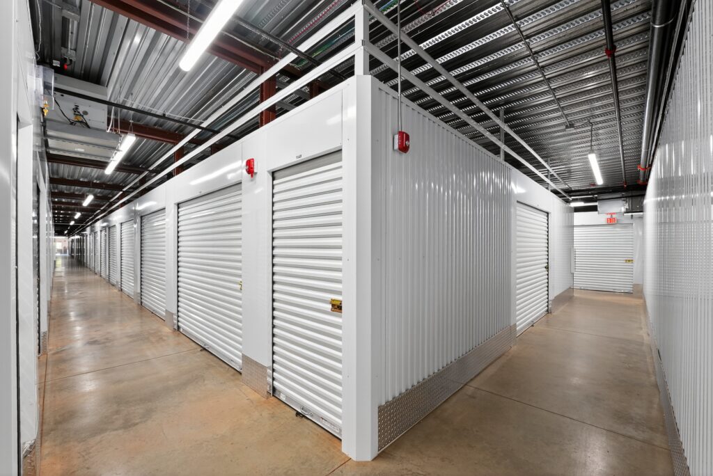 A hallway lined with white metal self-storage units featuring roll-up doors and concrete floors.