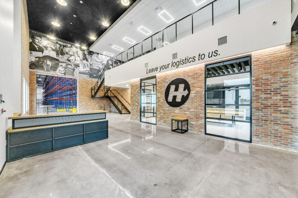 Modern office lobby with a brick wall, a black “H” logo, and a mural of historic delivery trucks.