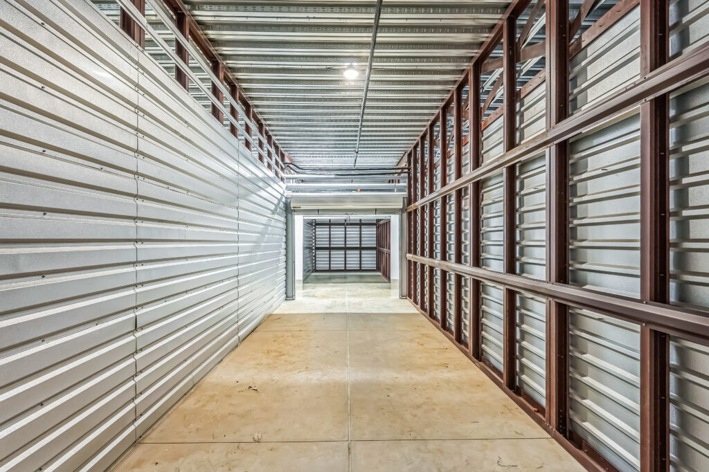 A long, empty corridor inside a self-storage facility with metal walls and an exposed ceiling structure.