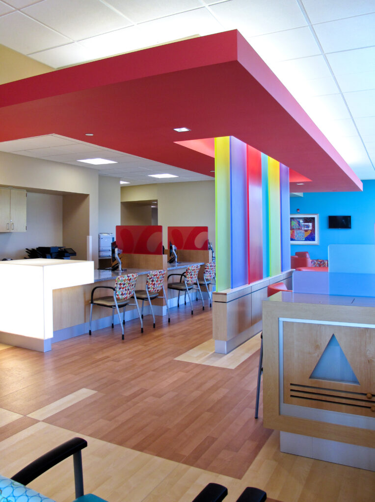 Modern office lobby with a reception desk, computer workstations, colorful vertical wall panels, and light wood flooring.