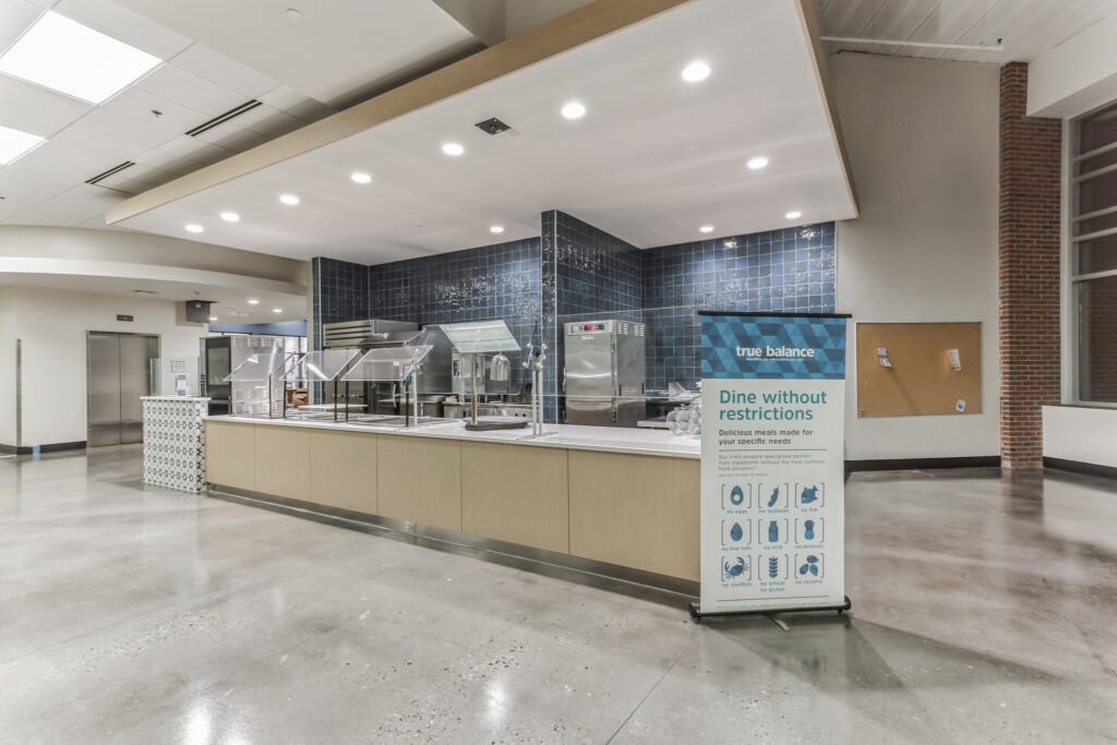 A serving counter in a dining facility next to a banner titled “True Balance” that lists common allergen-free food options.