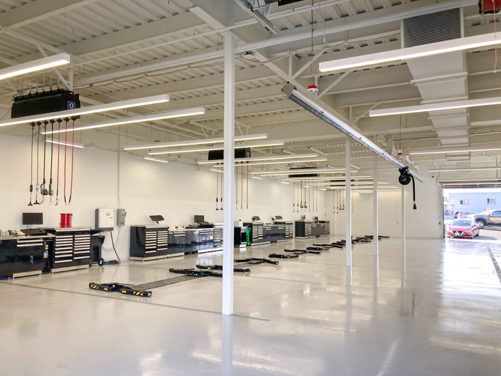 An empty, bright automotive repair shop with rows of workstations, tool cabinets, and vehicle lifts on a polished concrete floor.