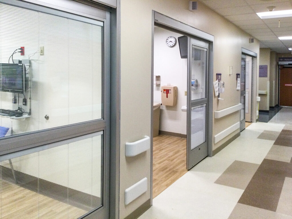 A hospital corridor with sliding doors leading into patient rooms.