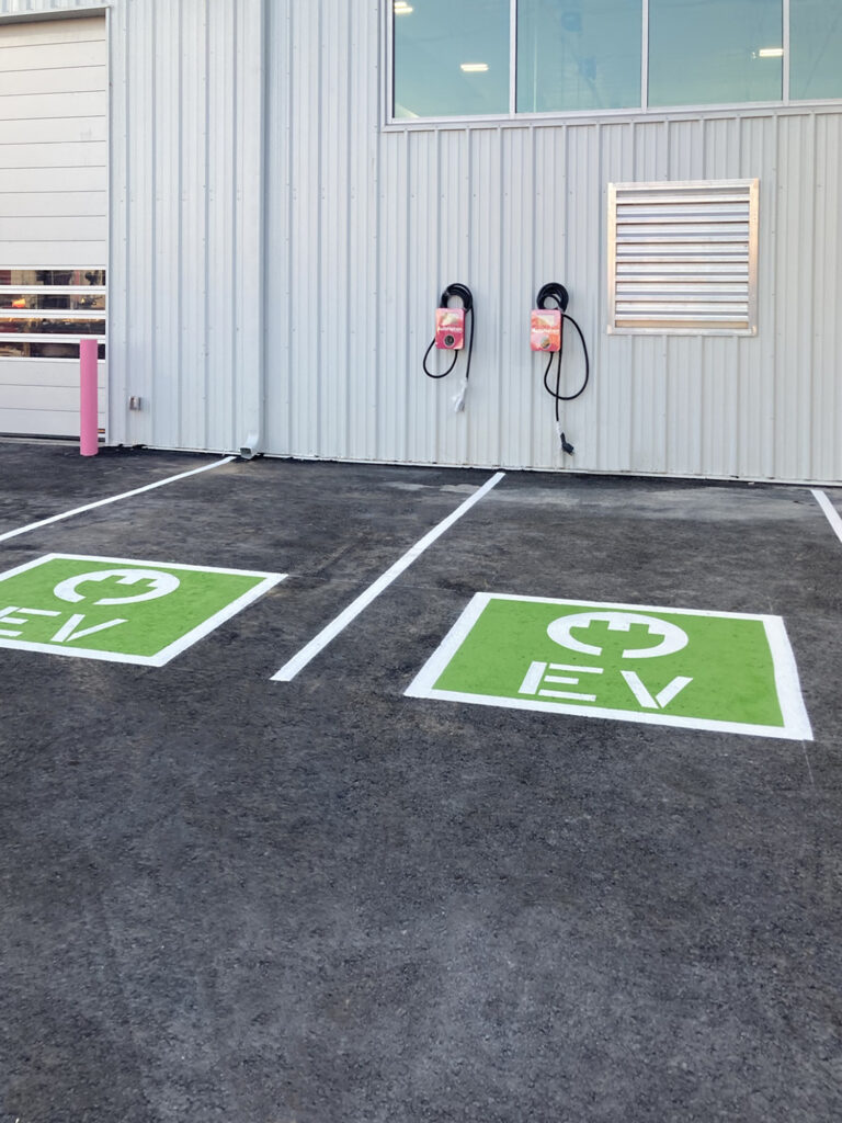 Two electric vehicle charging stations mounted on a building wall above two parking spaces marked with green and white EV symbols.