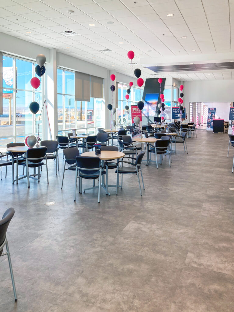 An empty cafe or event space featuring clusters of pink, black, and silver balloons tied to tables with black chairs.