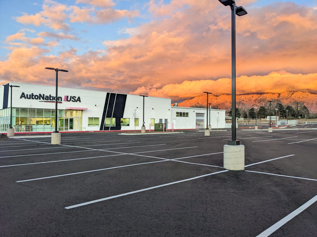 AutoNation USA dealership building with a vacant parking lot at sunset, set against a backdrop of mountains.