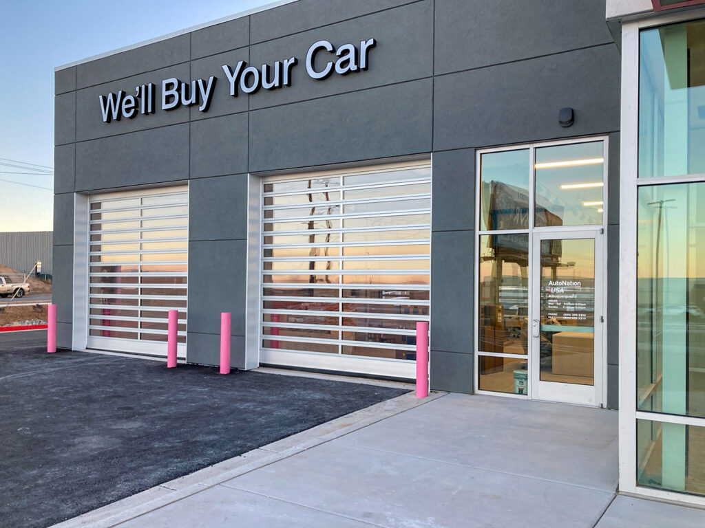 AutoNation USA building with the text “We’ll Buy Your Car” on the facade above two garage bays and a glass entrance door.
