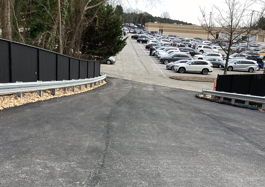 A paved driveway leading down to a large, crowded parking lot filled with various cars.