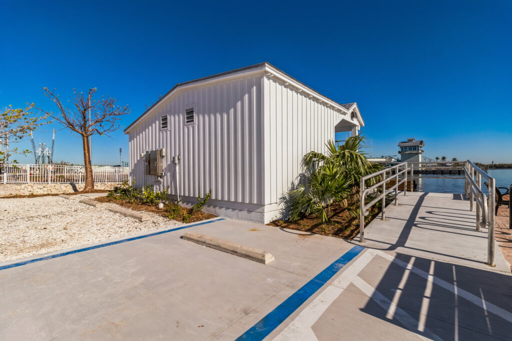 A white utility building next to a concrete walkway with metal railings overlooking a harbor.
