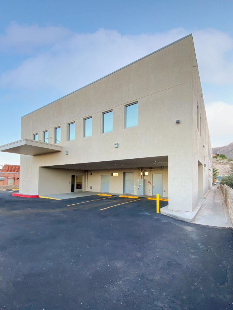A two-story commercial building with an open-air ground level featuring three doors and parking spaces.