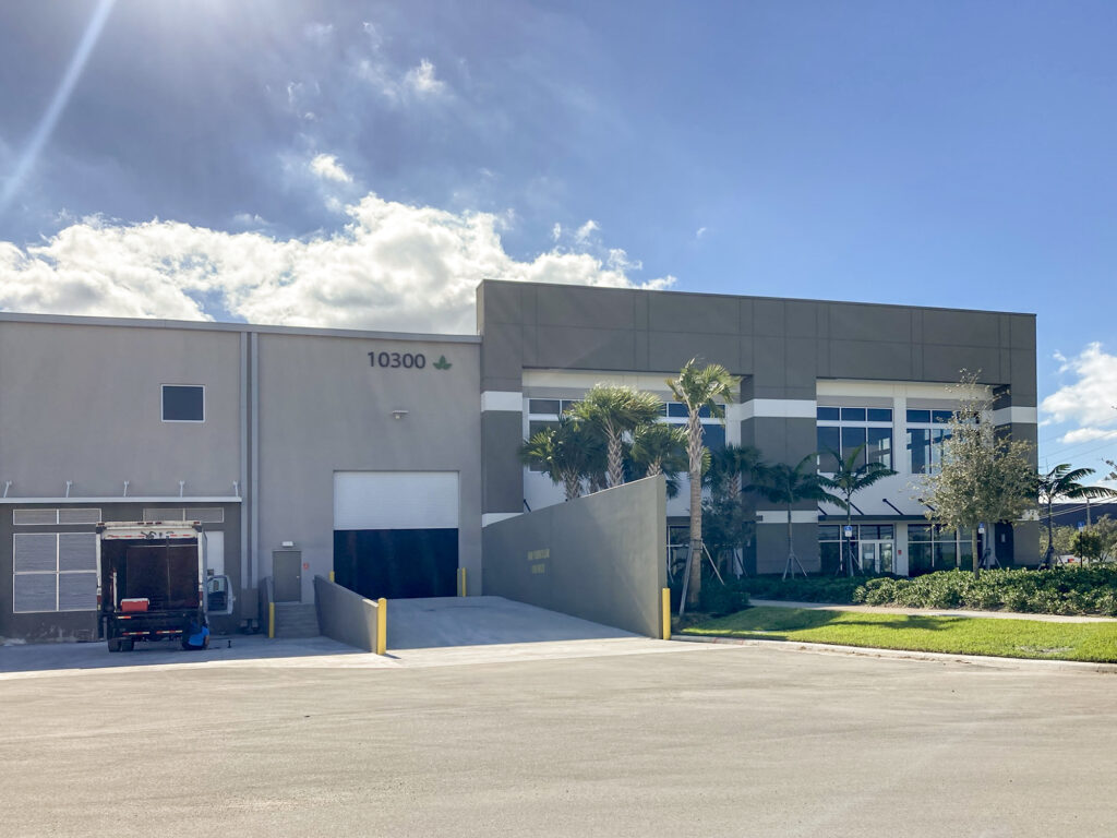 A commercial building with the address “10300” on the exterior, featuring a loading bay ramp and a parked delivery truck.