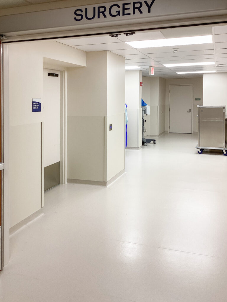 A hospital hallway entrance labeled “SURGERY,” leading to a corridor with medical equipment storage and doors.