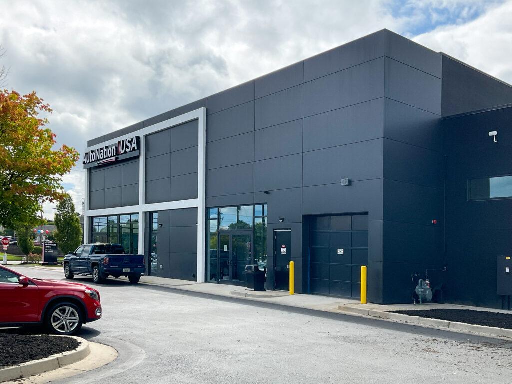 The exterior of an AutoNation USA dealership building with a blue pickup truck and a red SUV parked in front.