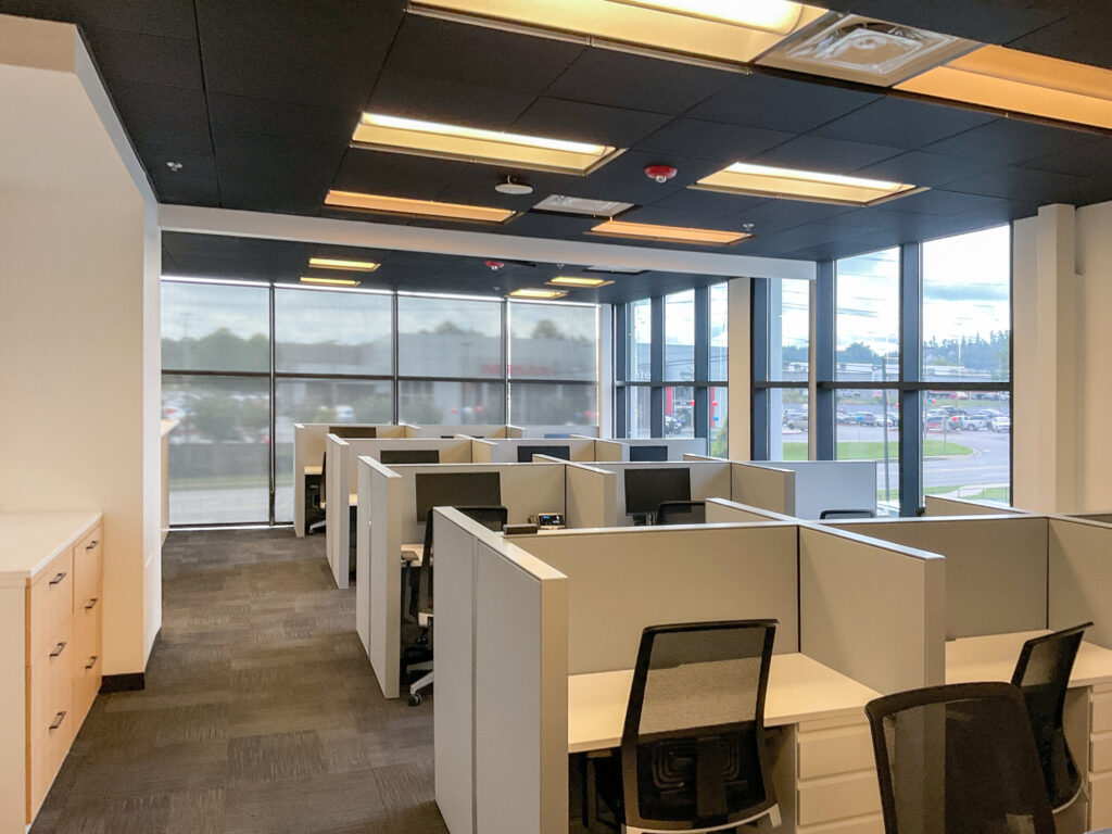 Office space with multiple grey cubicle workstations and black rolling chairs.