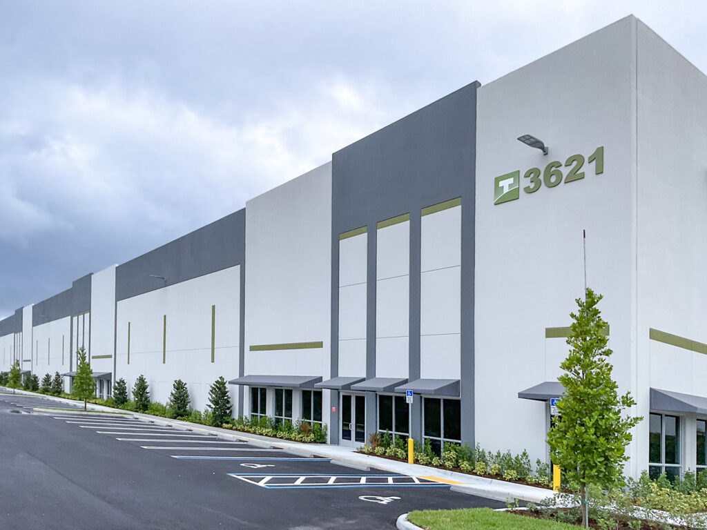 Modern commercial warehouse building with a gray and white exterior featuring the number 3621 and a green logo above the entrance.