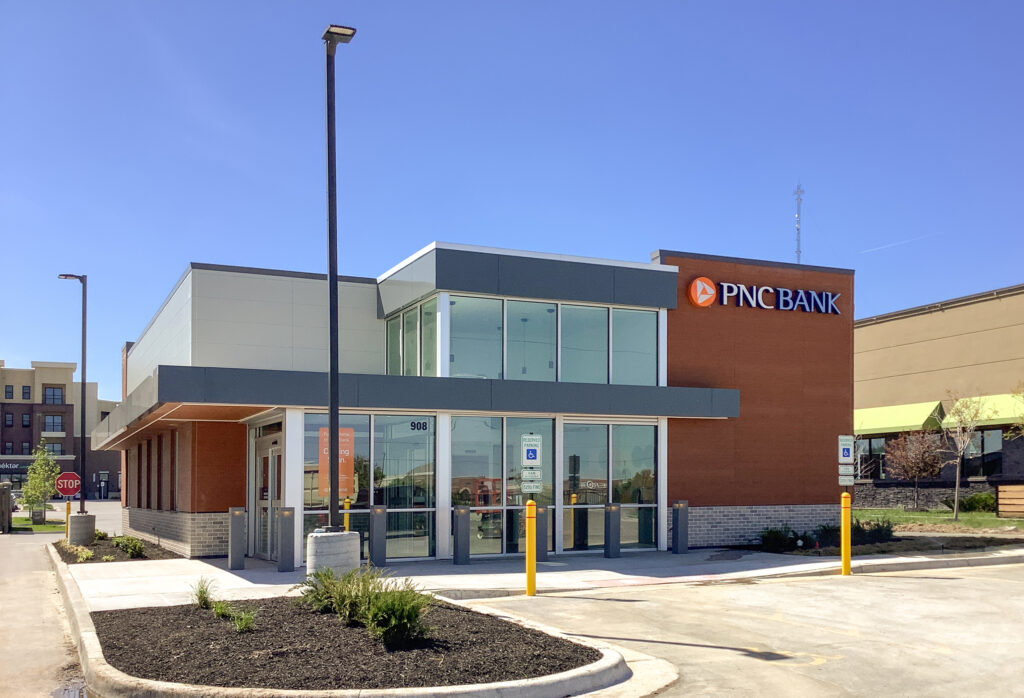 PNC Bank building with glass storefront and brown brick facade under a clear blue sky.