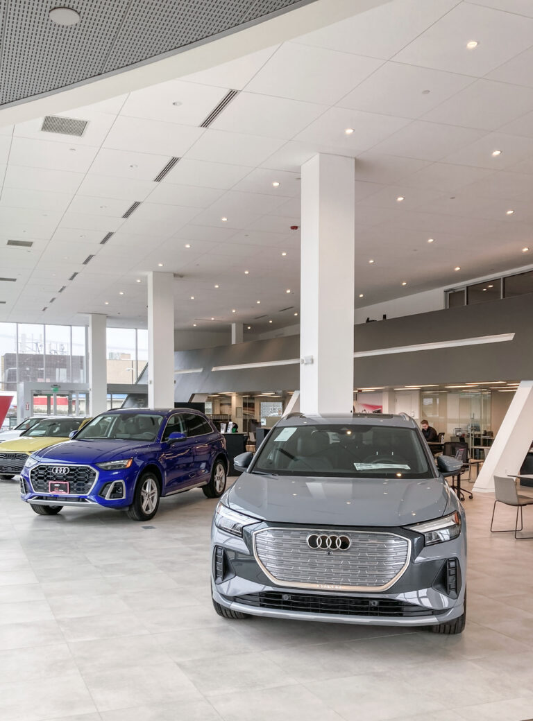 A gray Audi electric SUV in the foreground of a dealership showroom, with a blue Audi SUV parked behind it.