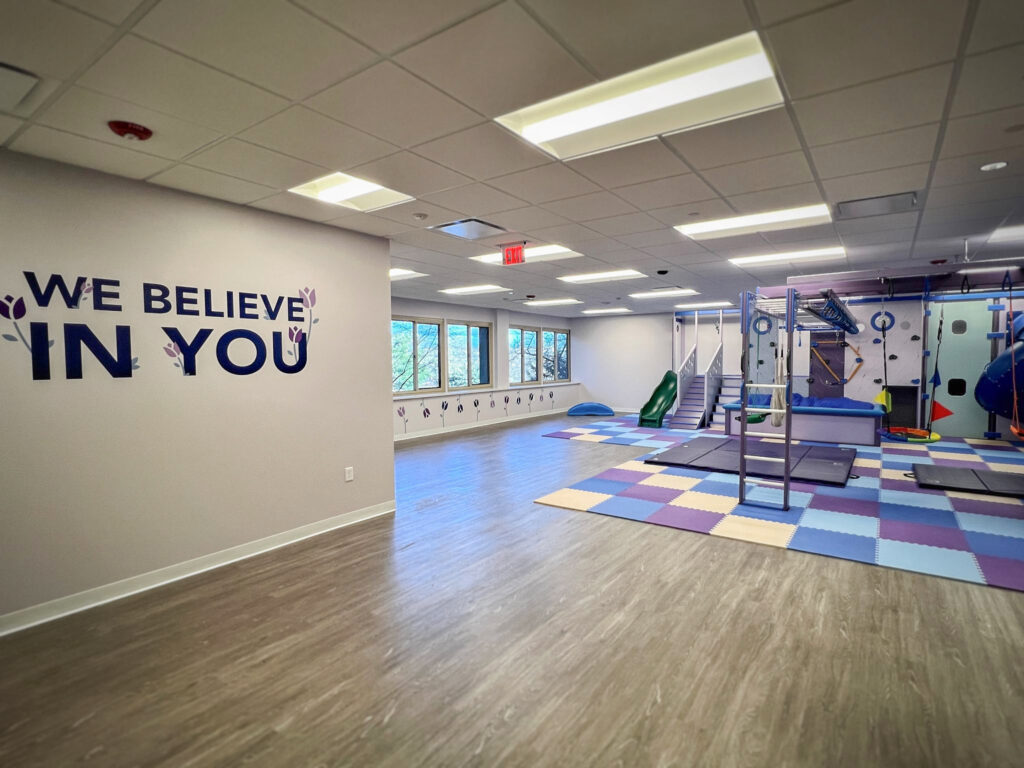 Indoor play area with foam floor mats, a climbing structure, and a wall decal that says “WE BELIEVE IN YOU.”