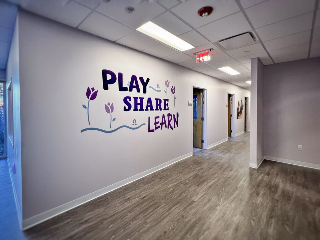 A hallway wall featuring the text “PLAY SHARE LEARN” in purple lettering with illustrations of tulips.