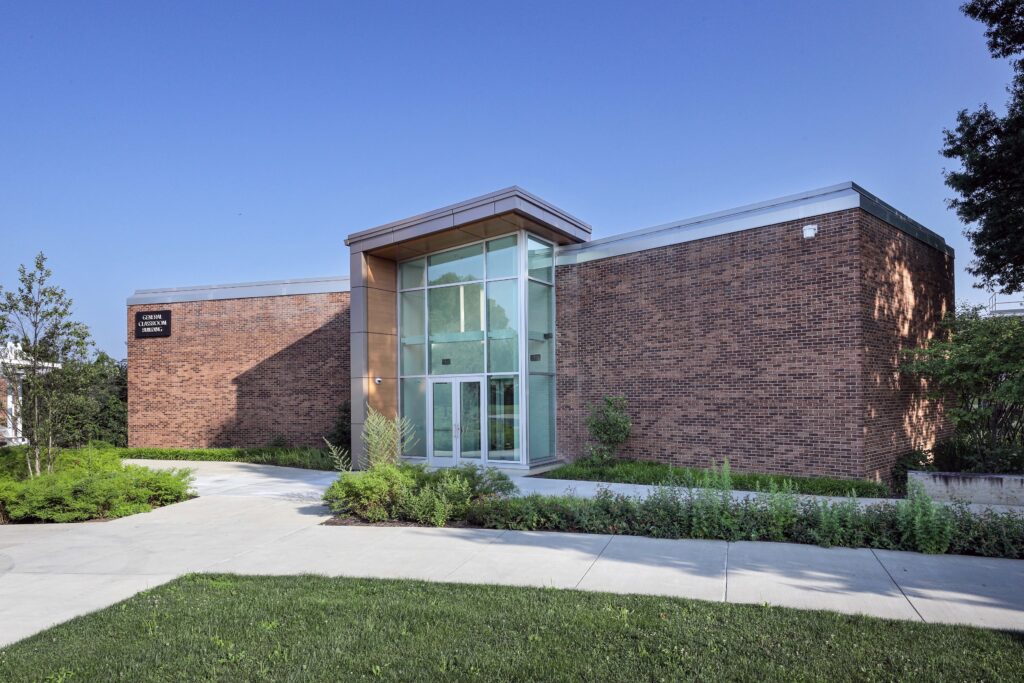 Exterior view of a one-story brick building labeled “General Classroom Building” with a glass entrance.