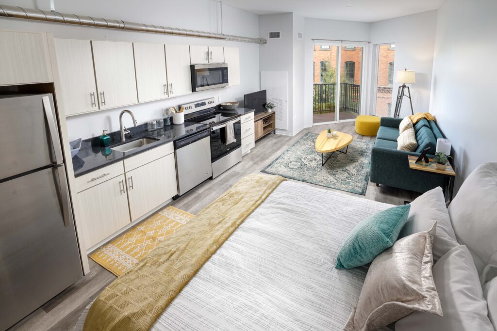 Studio apartment with an open-plan kitchen, living area with a blue sofa, and a bed in the foreground.