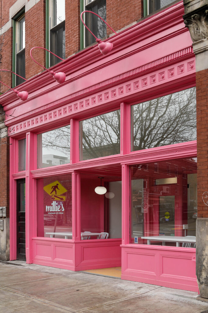 Storefront of Millie’s Homemade Ice Cream featuring a bright pink facade and large glass windows.