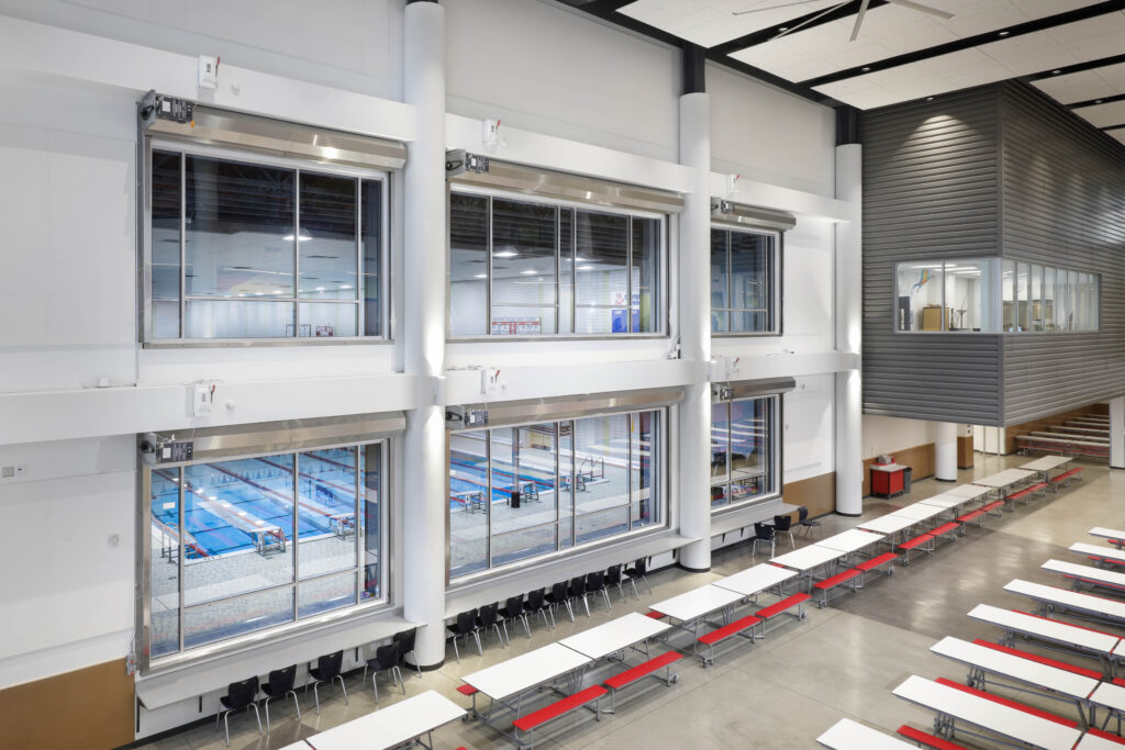 Large indoor space with rows of cafeteria tables looking through windows into an indoor swimming pool.