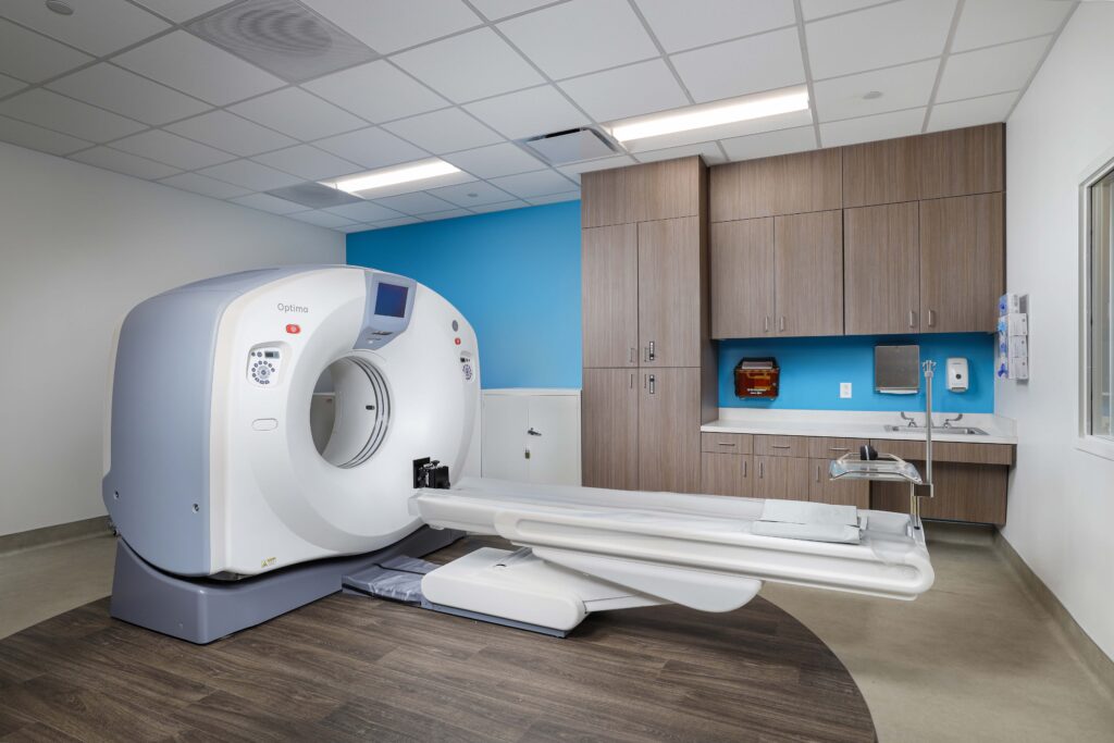 A CT scanner machine with an extendable patient table in a medical examination room.