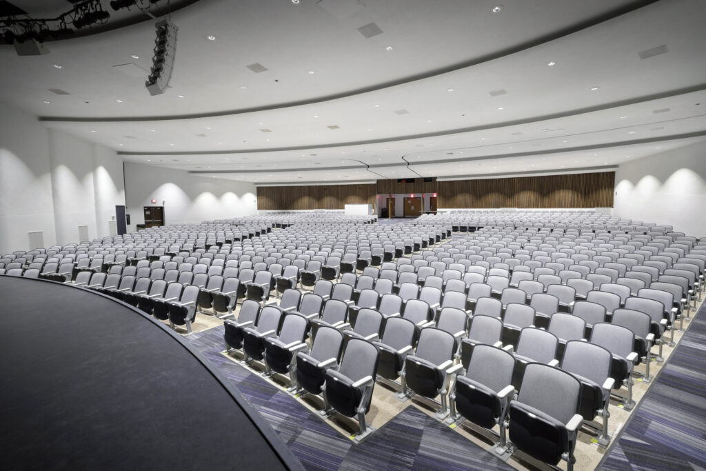 Large auditorium with rows of empty gray theater seats facing a stage.