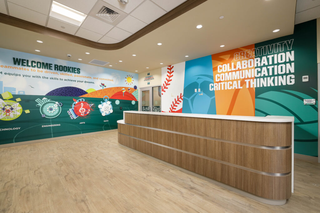 A reception area with a wooden desk and walls decorated with colorful murals featuring words like “Creativity,” “Collaboration,” and “Engineering.”