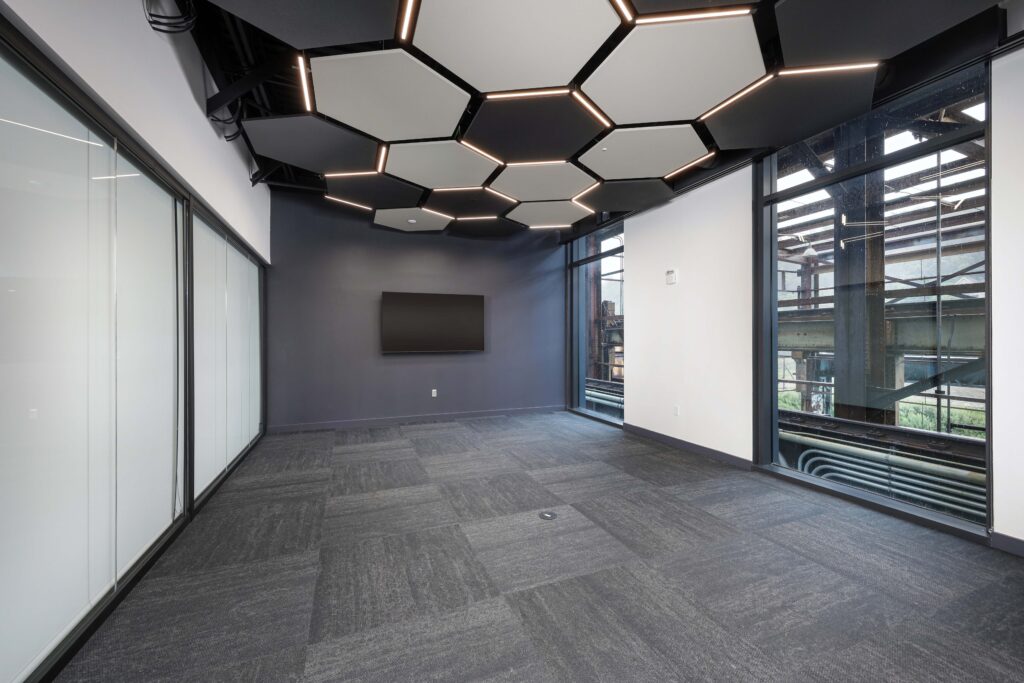Empty office space with a dark gray accent wall, wall-mounted television, and a hexagonal ceiling light fixture.