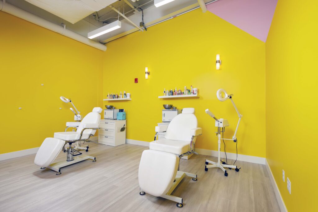Two white treatment chairs with adjustable lamps in a room with bright yellow walls.