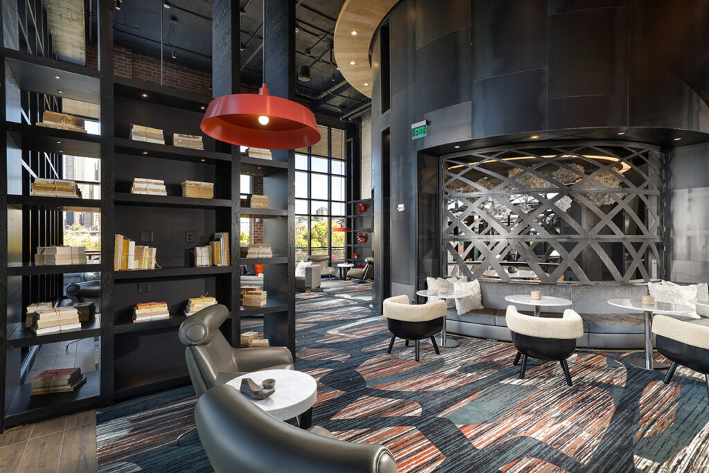 Lounge area with dark shelving filled with books, a red pendant light, patterned carpet, and curved seating booths.