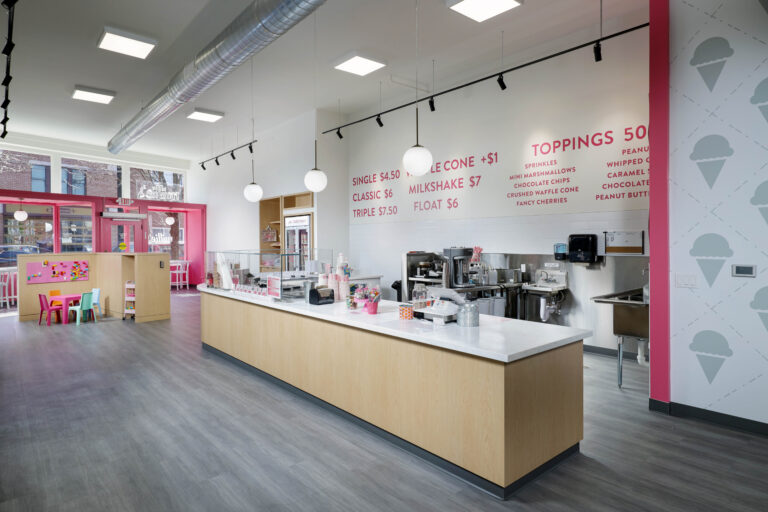 The interior of an ice cream shop with a long service counter and a menu printed on the back wall.