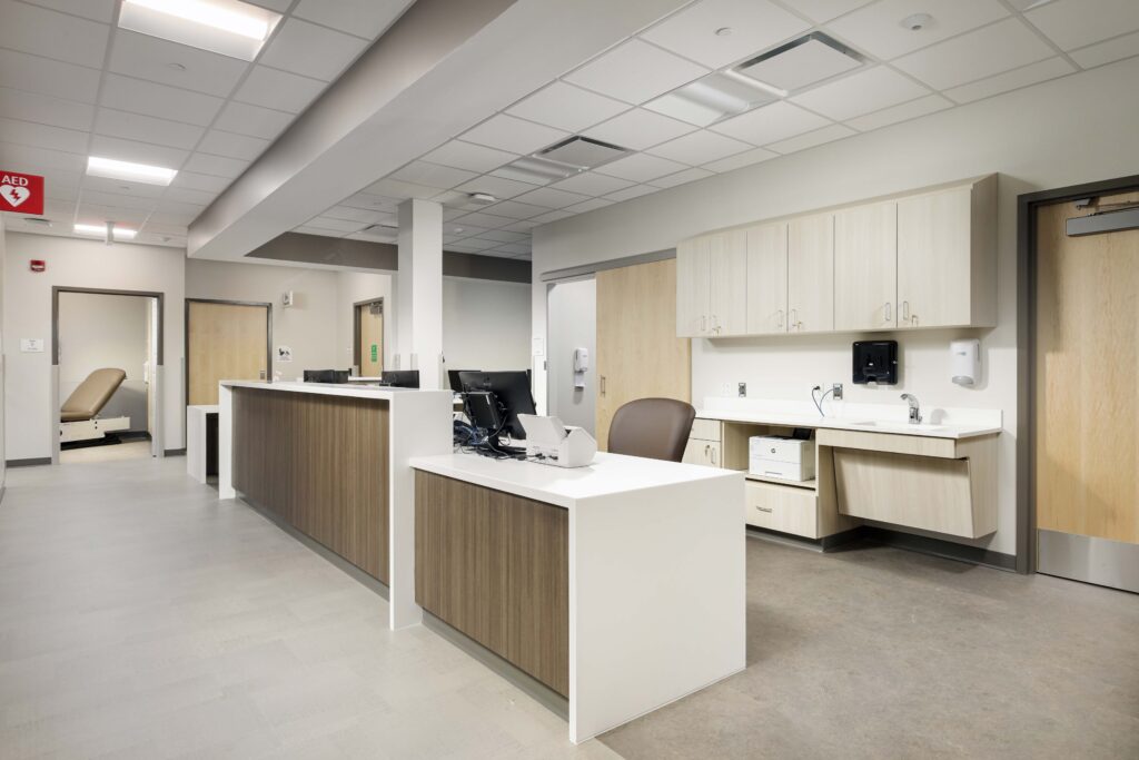Reception desk in a medical office with computer equipment, cabinets, and a doorway leading to an exam room.