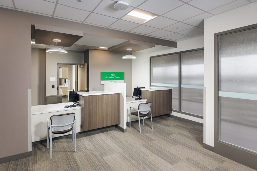 Reception desk at the AHN Outpatient Center with two workstations, chairs, and frosted glass partitions.