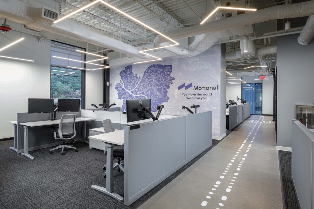 Modern office space with cubicles, a floor graphic of dashed lines, and a wall mural featuring a stylized map and the Motional company logo.