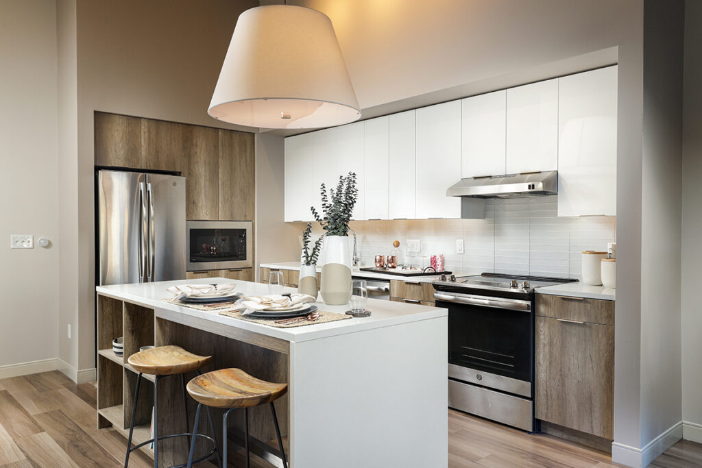 Modern kitchen with white and wood cabinets, stainless steel appliances, and a center island with two wooden stools.