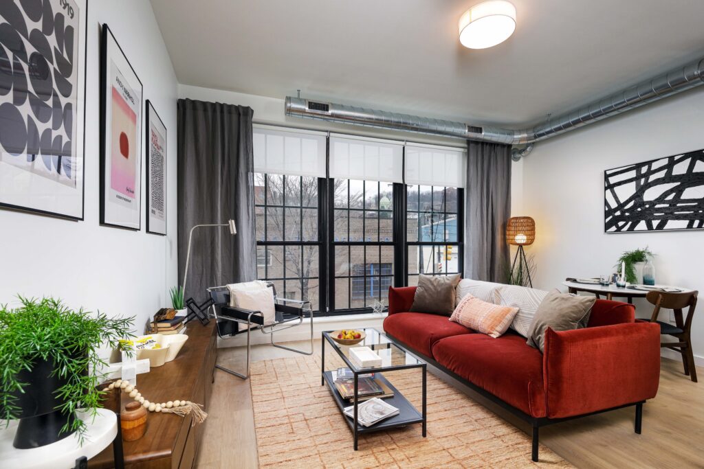 Living room with a red velvet sofa, black metal-framed armchair, glass coffee table, and a large window overlooking a street.