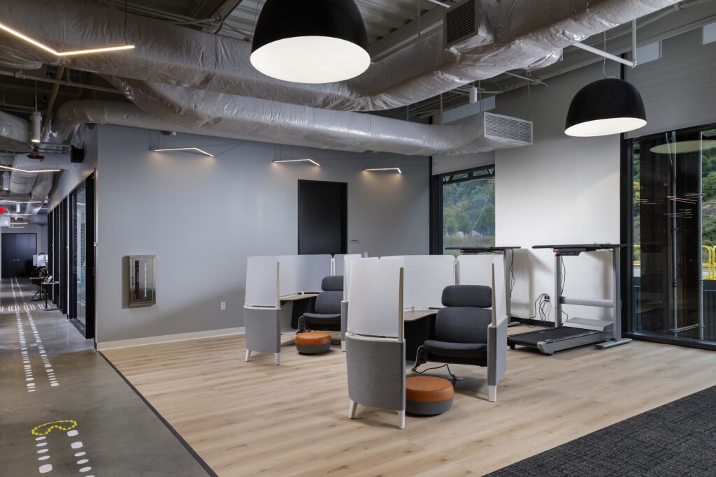 An open office space with two armchairs behind privacy screens, a treadmill desk, and exposed ceiling ductwork.