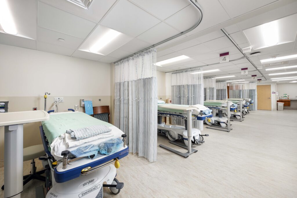 A hospital ward with several medical gurneys separated by privacy curtains.