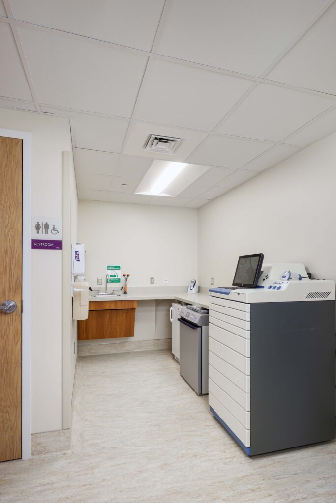 A medical office featuring a sink, an under-counter dishwasher, and a tall medical equipment cabinet with a screen on top.
